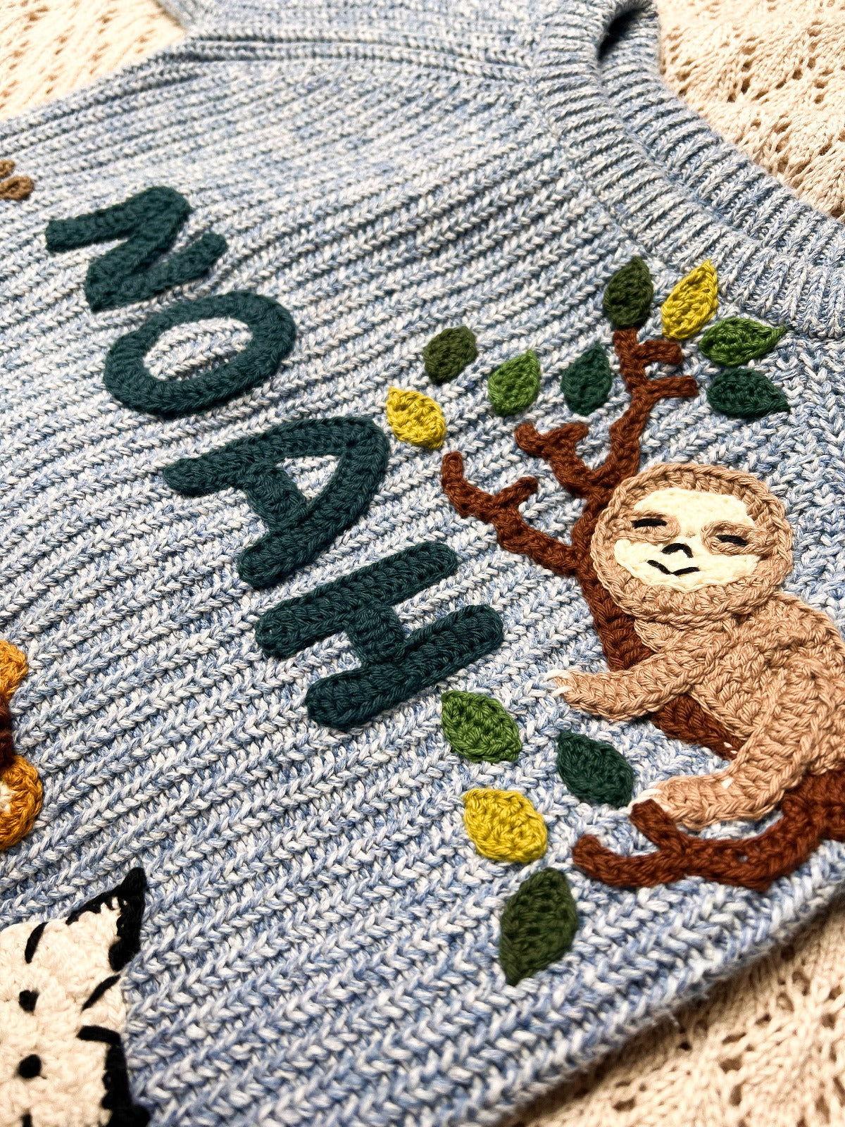 Blue handknitted jumper and the word Noah with a crochet sloth