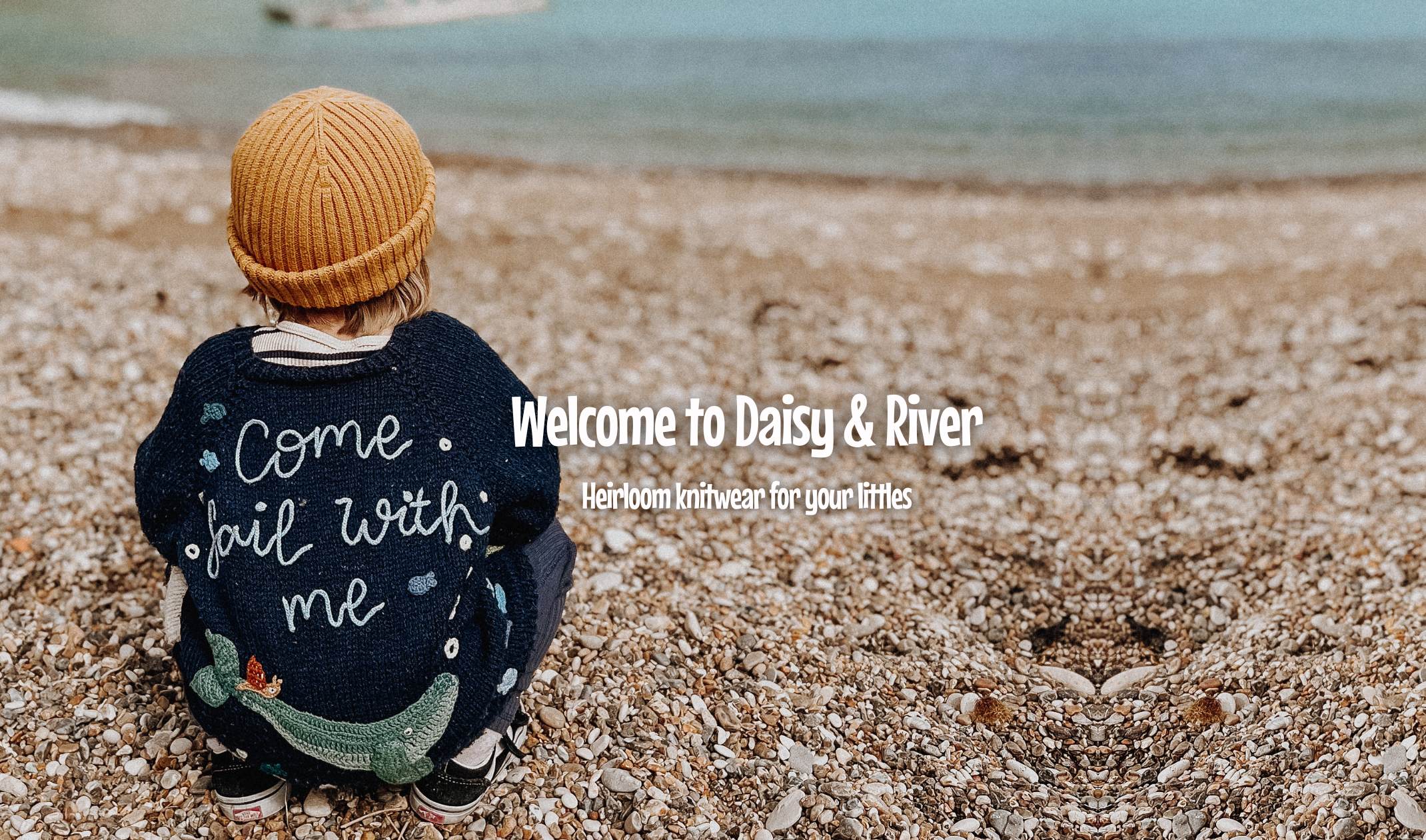 toddler on a beach wearing a navy handknitted cardigan with the words come sail with me